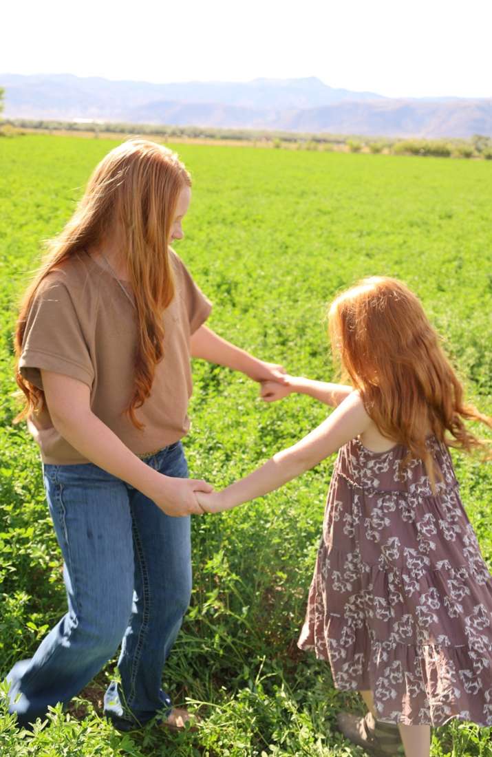 The girls holding hands in an alfalfa field with the mountains behind